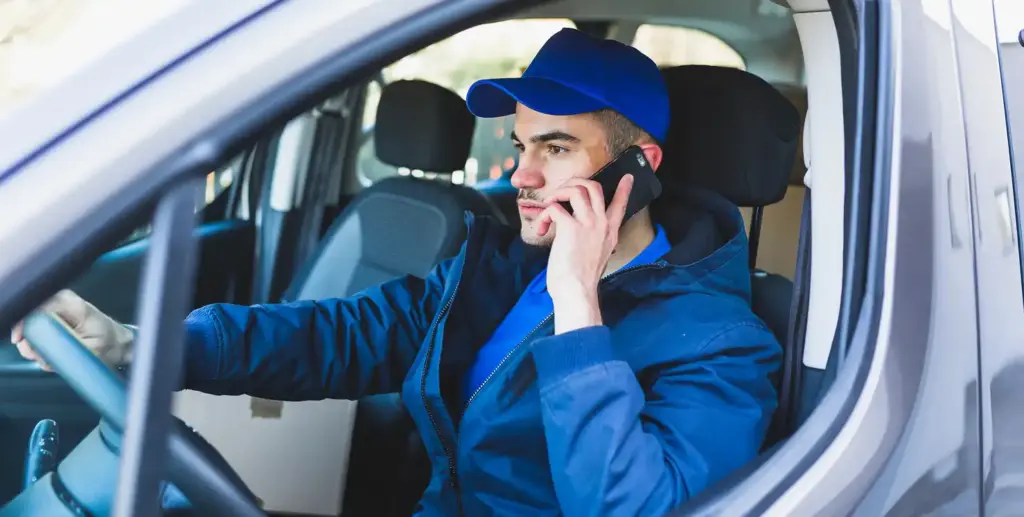 Servicetechnicus die in een werkvoertuig rijdt terwijl hij aan de telefoon spreekt over een afspraak voor thuisreparatie.